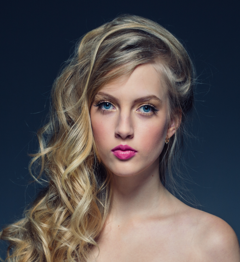 Blonde woman with long, wavy hair and bold pink lips, showcasing a glamorous hairstyle, representing expert hair services at Kylie Studio Salon in Bethesda, MD.